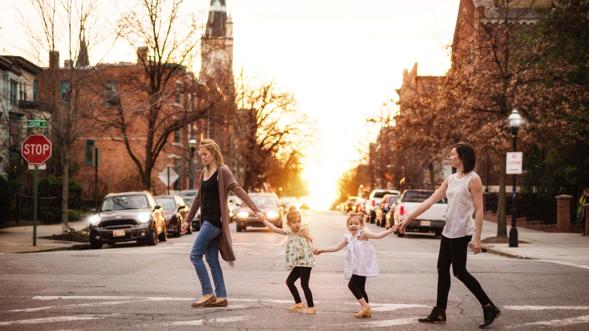 Two moms and two kids walking across city street Golding hands. Image for Worthy Threads, a unique toddler clothing brand.