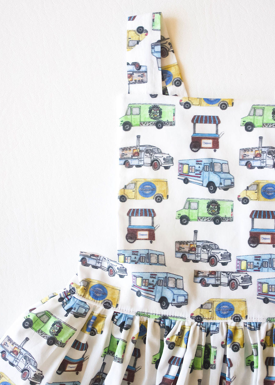 Close up of girls pinafore dress featuring food trucks.  First custom print by Worthy Threads, a unique toddler clothing brand.